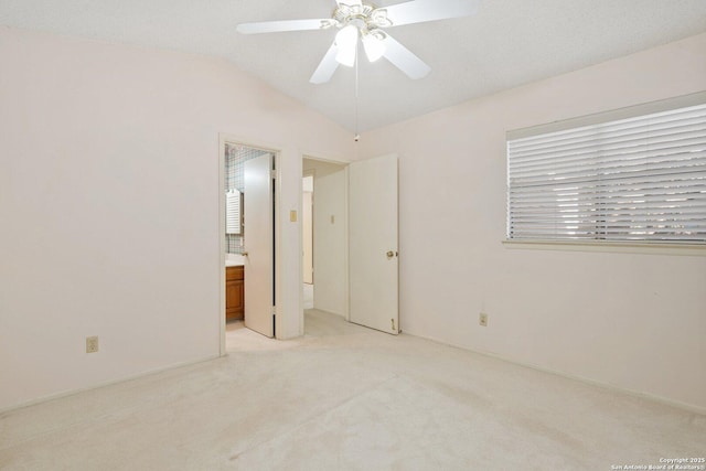 unfurnished bedroom with a ceiling fan, lofted ceiling, light colored carpet, and connected bathroom