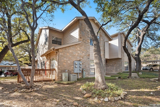 view of property exterior featuring stone siding, a wooden deck, and central air condition unit