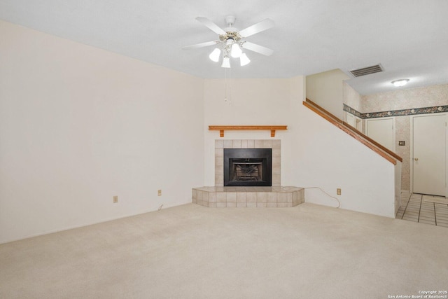 unfurnished living room featuring carpet, a tile fireplace, visible vents, and a ceiling fan