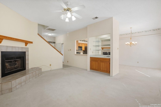 unfurnished living room featuring ceiling fan with notable chandelier, visible vents, a tiled fireplace, and light colored carpet