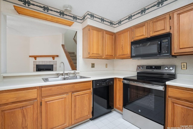 kitchen featuring light countertops, brown cabinetry, a sink, a textured ceiling, and black appliances