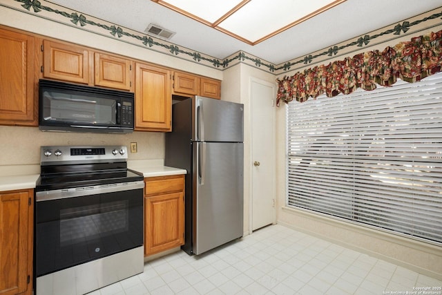 kitchen with stainless steel appliances, brown cabinetry, light countertops, and visible vents