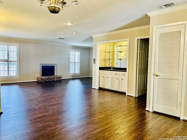 unfurnished living room featuring sink, ornamental molding, dark wood-type flooring, and a brick fireplace