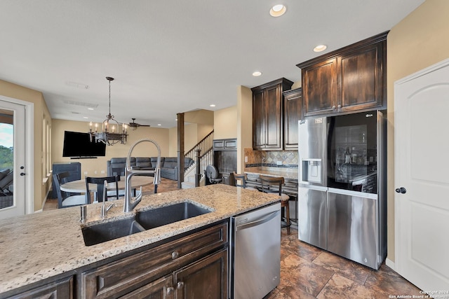 kitchen with stainless steel appliances, dark brown cabinetry, light stone counters, decorative light fixtures, and sink