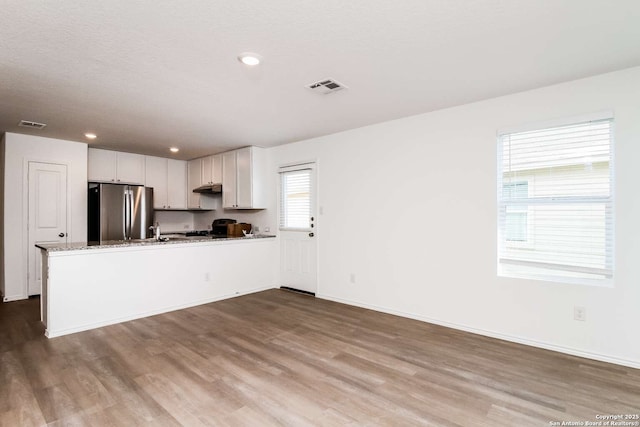 kitchen featuring light stone countertops, white cabinets, light hardwood / wood-style floors, stainless steel fridge, and kitchen peninsula