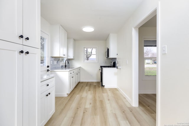 kitchen featuring appliances with stainless steel finishes, sink, backsplash, light hardwood / wood-style floors, and white cabinets