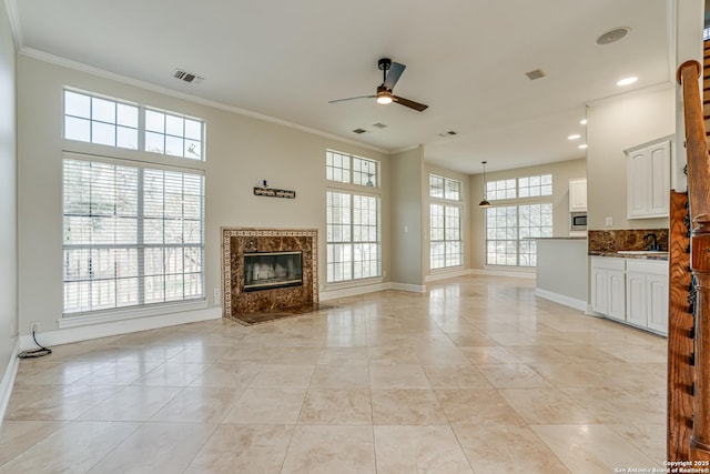 unfurnished living room featuring a premium fireplace, sink, light tile patterned flooring, ceiling fan, and crown molding