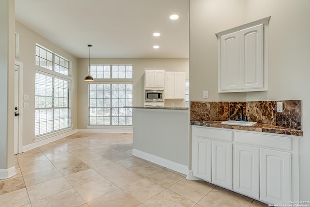 kitchen with hanging light fixtures, white cabinets, stainless steel microwave, sink, and kitchen peninsula