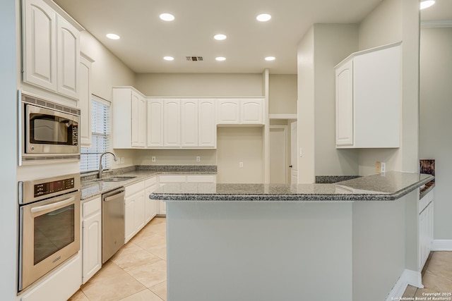 kitchen featuring white cabinetry, kitchen peninsula, stainless steel appliances, sink, and dark stone counters