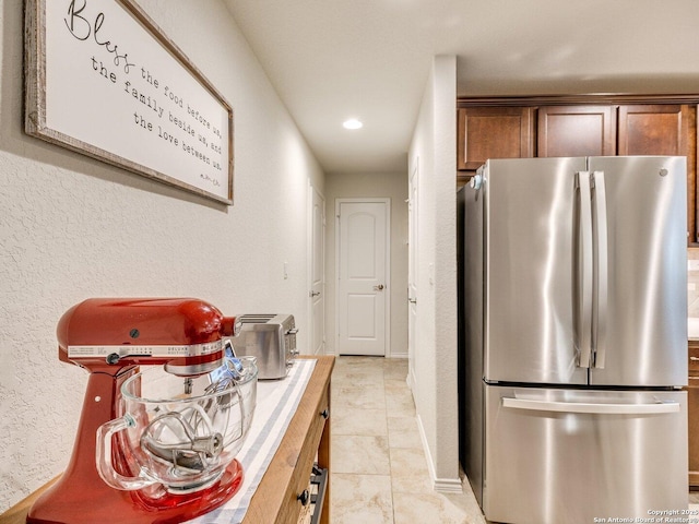 kitchen featuring a textured wall, light countertops, freestanding refrigerator, and brown cabinets