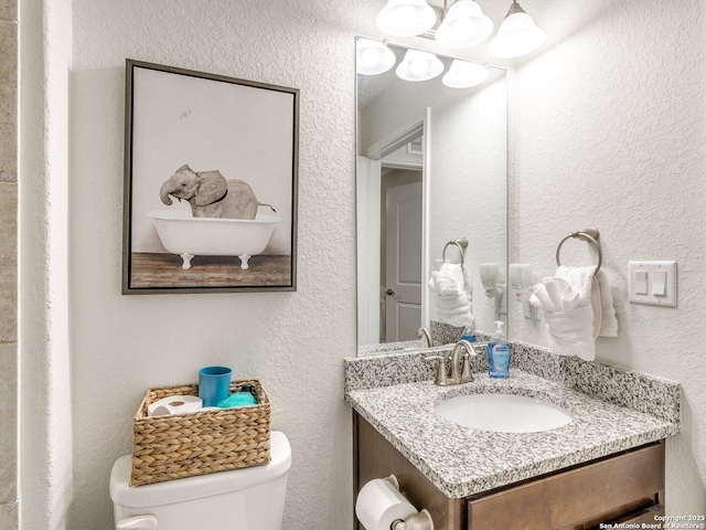 bathroom with toilet, a textured wall, and vanity