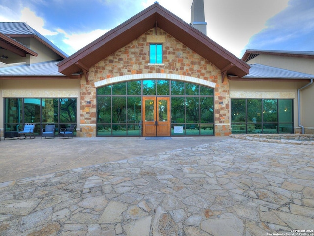 view of exterior entry with a patio area, stone siding, a chimney, and stucco siding