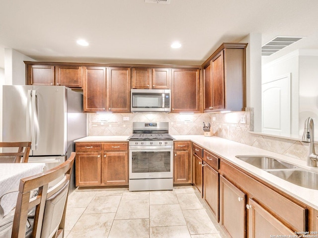 kitchen featuring appliances with stainless steel finishes, brown cabinets, light countertops, and a sink