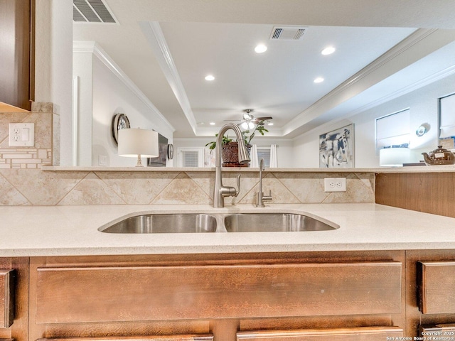 kitchen with a raised ceiling, light countertops, visible vents, backsplash, and a sink