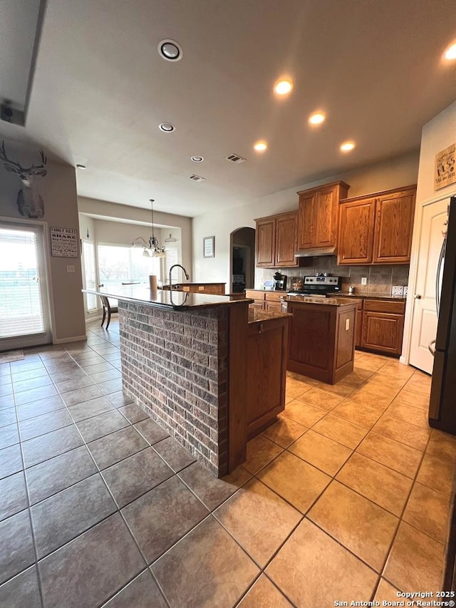 kitchen with an island with sink, stainless steel range with electric cooktop, black fridge, and tile patterned floors