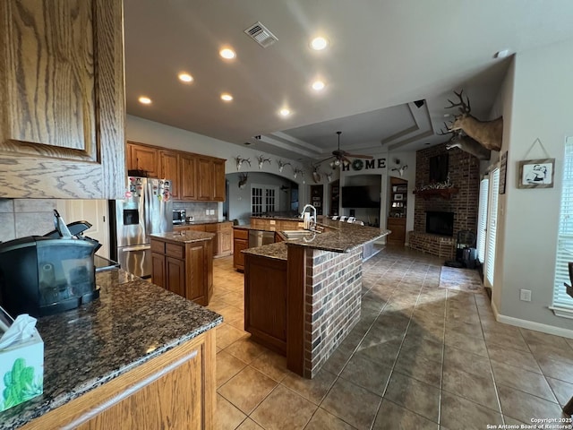 kitchen featuring a tray ceiling, dark stone counters, a large island, stainless steel appliances, and a fireplace