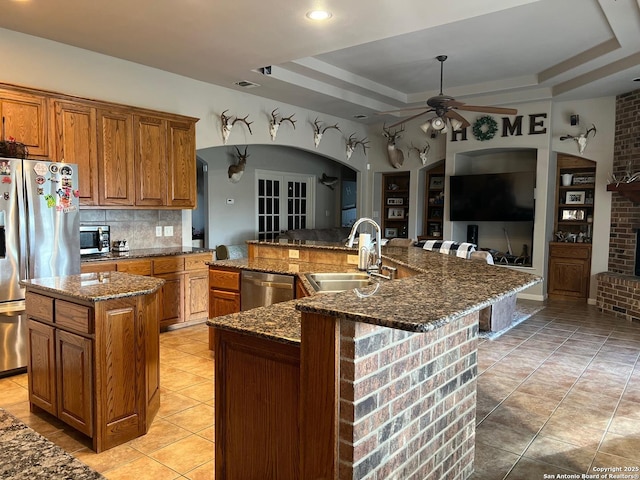 kitchen featuring stainless steel appliances, a large island with sink, a tray ceiling, sink, and dark stone countertops