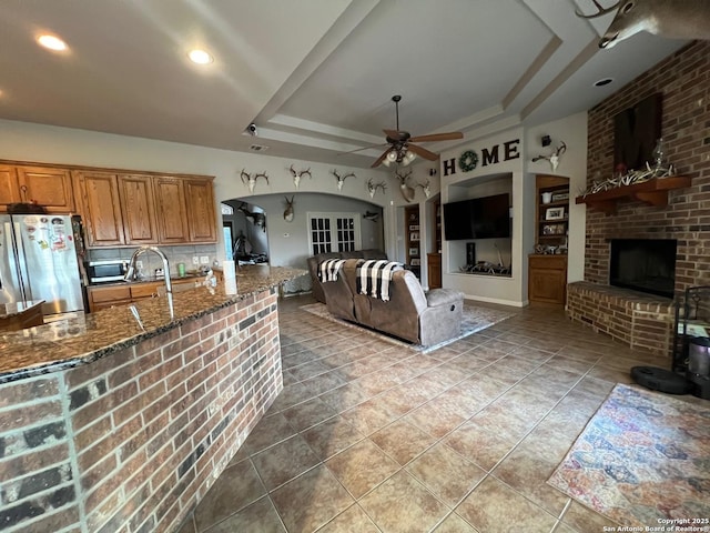 kitchen featuring a fireplace, ceiling fan, stainless steel appliances, and a raised ceiling