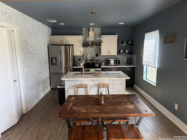 kitchen with sink, stainless steel appliances, dark hardwood / wood-style flooring, hanging light fixtures, and an island with sink