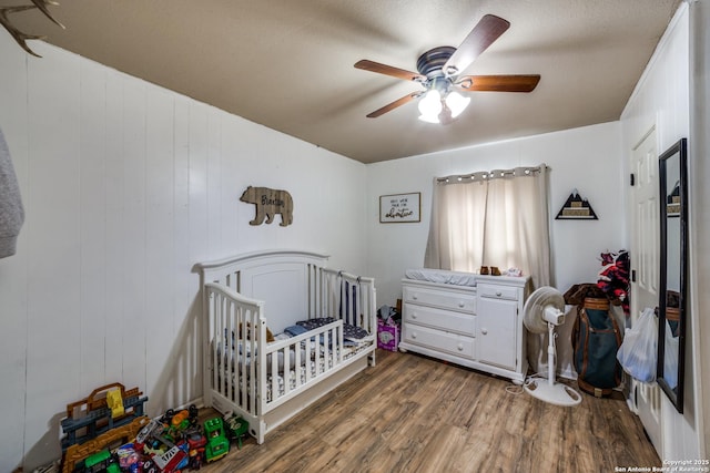 bedroom with a crib, ceiling fan, and dark hardwood / wood-style floors