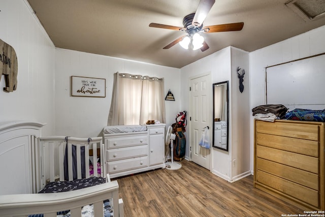 bedroom featuring a crib, hardwood / wood-style flooring, and ceiling fan