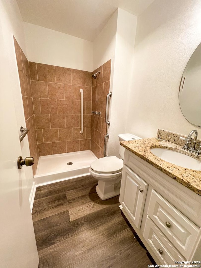 bathroom featuring toilet, vanity, hardwood / wood-style floors, and a tile shower