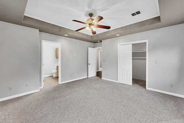 unfurnished bedroom featuring a closet, a tray ceiling, ceiling fan, connected bathroom, and light carpet
