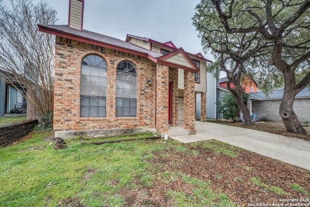 view of front of property featuring a front yard, concrete driveway, brick siding, and a chimney