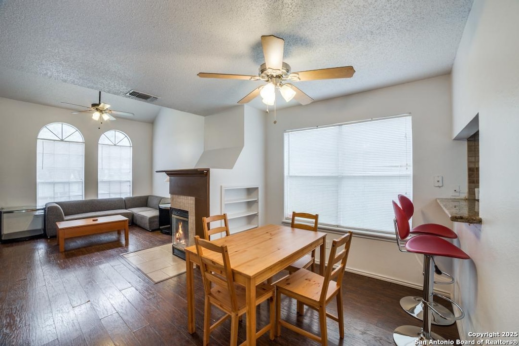 dining space featuring a glass covered fireplace, visible vents, dark wood finished floors, and a textured ceiling