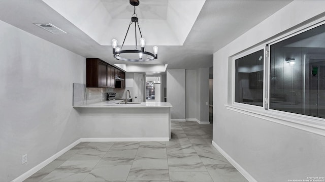 kitchen featuring kitchen peninsula, an inviting chandelier, sink, a tray ceiling, and dark brown cabinets