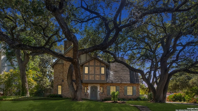 english style home featuring brick siding, a chimney, and a front yard