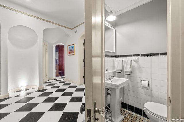 half bath featuring tile walls, visible vents, toilet, ornamental molding, and tile patterned floors