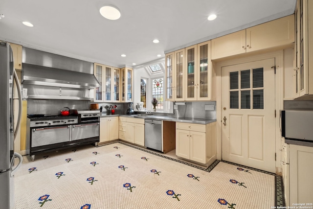 kitchen with recessed lighting, stainless steel appliances, a sink, wall chimney range hood, and stainless steel counters