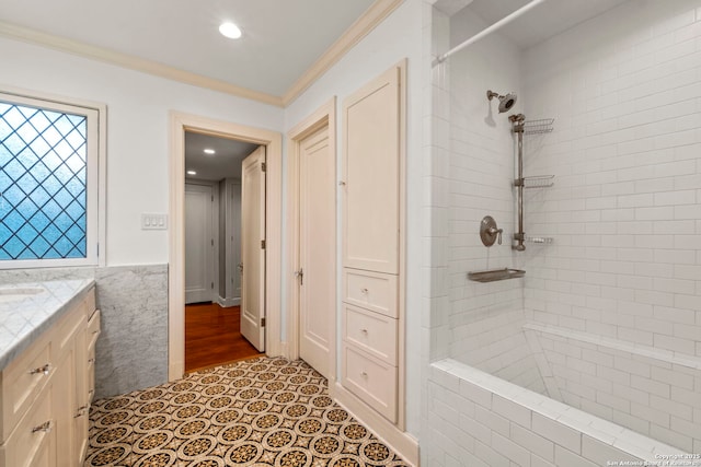 full bath featuring a wainscoted wall, tile patterned flooring, a tile shower, crown molding, and vanity