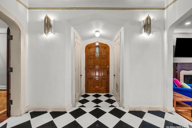 foyer featuring arched walkways, baseboards, and tile patterned floors