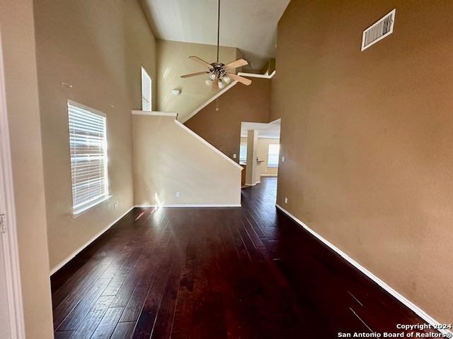 unfurnished living room with ceiling fan, a towering ceiling, and dark hardwood / wood-style flooring