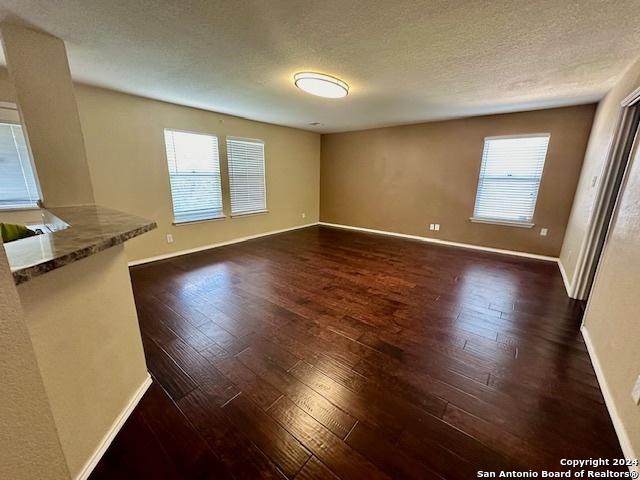 unfurnished living room with a healthy amount of sunlight, a textured ceiling, and dark hardwood / wood-style flooring