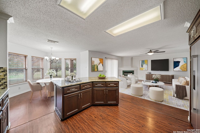 kitchen with dark brown cabinets, dark hardwood / wood-style flooring, light stone counters, and decorative light fixtures