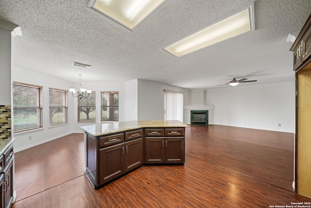 kitchen with pendant lighting, a kitchen island, light stone counters, dark wood-type flooring, and ceiling fan with notable chandelier