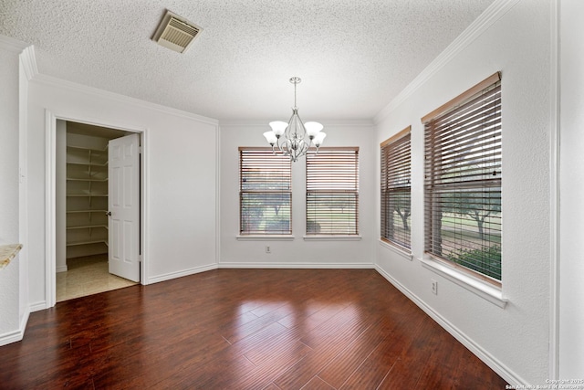 empty room featuring a textured ceiling, dark hardwood / wood-style floors, crown molding, and a chandelier