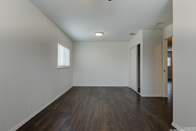 spare room featuring a textured ceiling, dark wood finished floors, visible vents, and baseboards