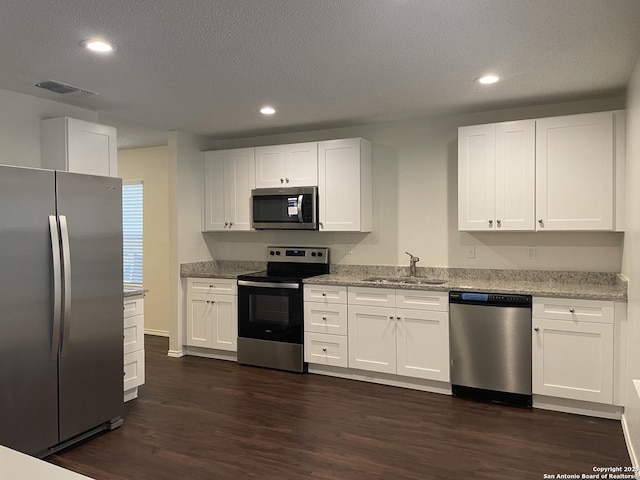 kitchen with a sink, white cabinets, appliances with stainless steel finishes, light stone countertops, and dark wood finished floors