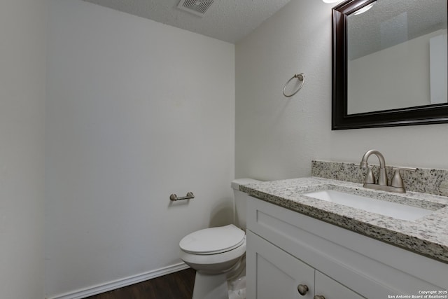 bathroom featuring a textured ceiling, toilet, wood finished floors, vanity, and visible vents