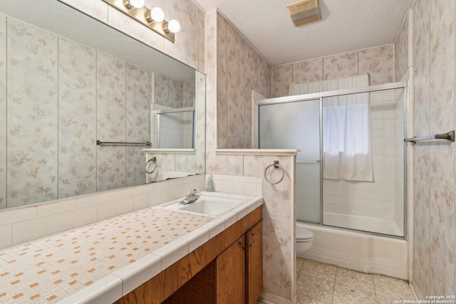 bathroom with a textured ceiling, toilet, shower / bath combination with glass door, vanity, and wallpapered walls