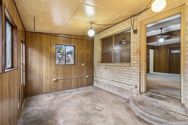 unfurnished room featuring brick wall, wood walls, and unfinished concrete floors