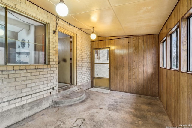 interior space featuring brick wall, unfinished concrete floors, and wooden walls