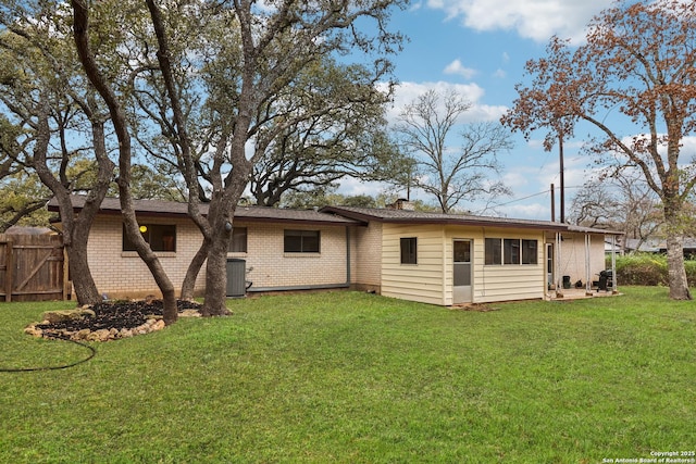 rear view of house with central AC unit, brick siding, a lawn, and a chimney