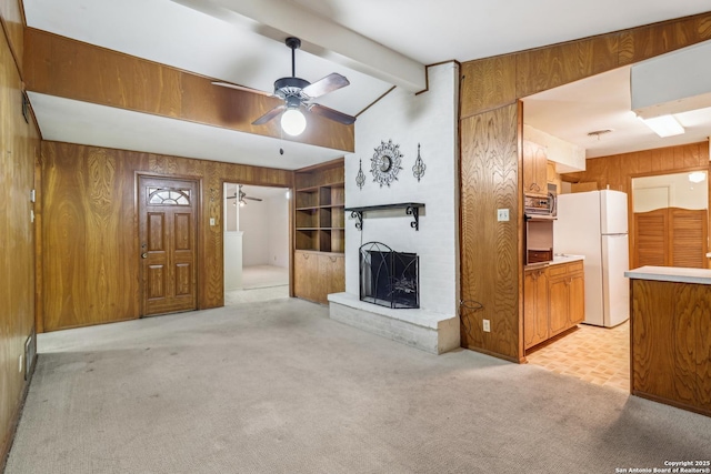 unfurnished living room with a fireplace, light colored carpet, lofted ceiling with beams, wood walls, and ceiling fan