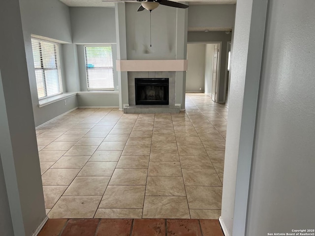 unfurnished living room with ceiling fan, light tile patterned flooring, and a tile fireplace