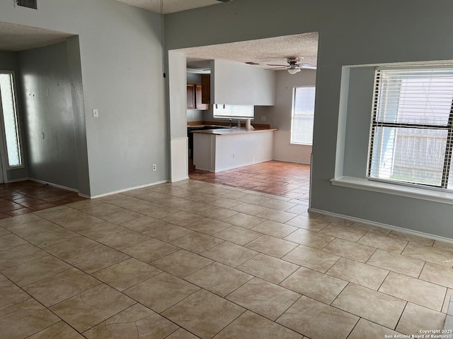 unfurnished living room featuring a textured ceiling, ceiling fan, and light tile patterned floors